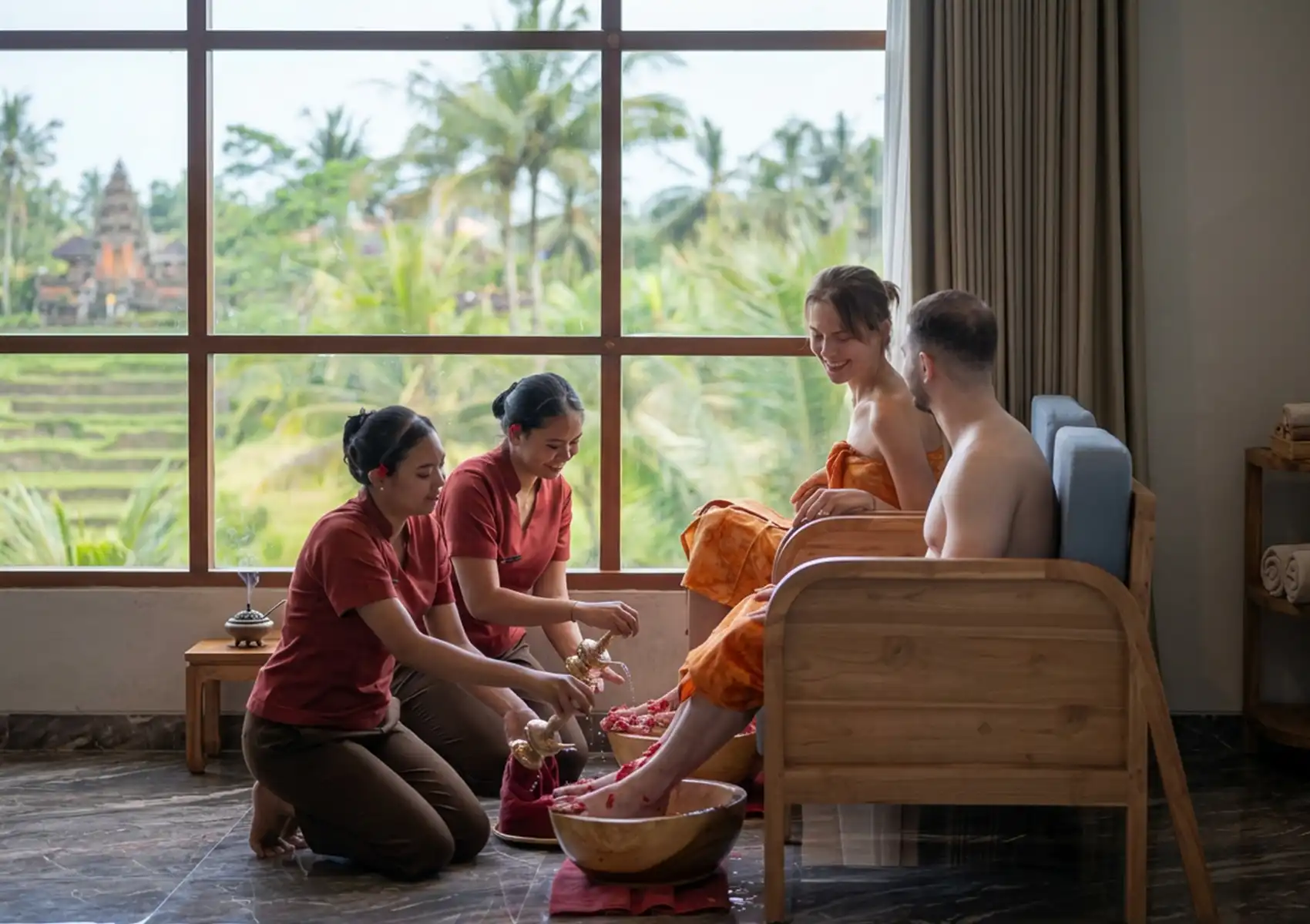 Serene tropical spa with attendants in red uniforms giving foot baths in golden bowls to guests wrapped in orange towels, overlooking palm trees and rice terraces.